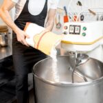 Liquidation matériel boulangerie – un professionnel verse de la farine dans un pétrin industriel dans un atelier moderne