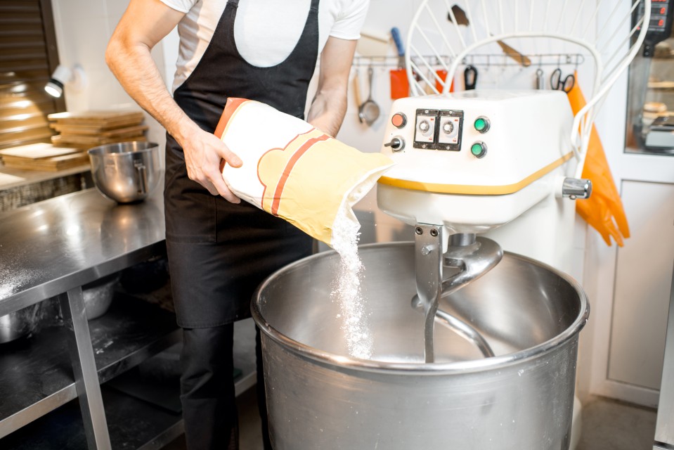 Liquidation matériel boulangerie – un professionnel verse de la farine dans un pétrin industriel dans un atelier moderne